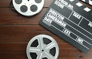 Movie clapper and film reels on wooden table, flat lay