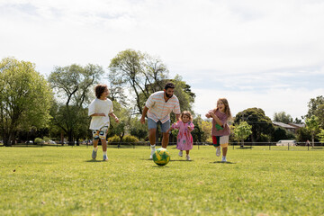 Dad with his kids playing soccer in a park