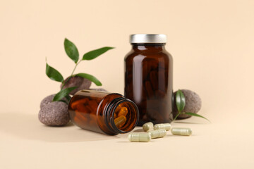 Medical bottles with pills, stones and green leaves on beige background