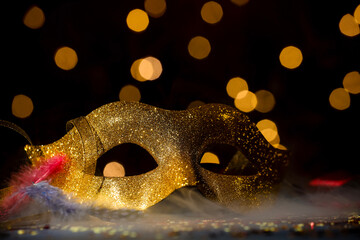 Beautiful carnival mask and confetti in smoke on dark background with blurred lights, closeup