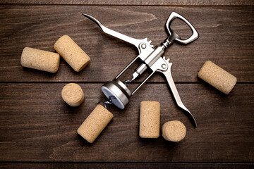 Wing corkscrew and corks on wooden table, flat lay