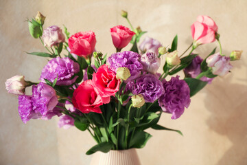 Vase with beautiful eustoma flowers near beige wall, closeup