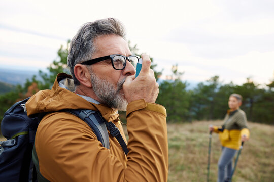 Man with asthma takes a dose of an inhaler on a mountain