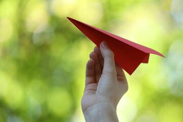 Woman with handmade paper plane on blurred green background, closeup