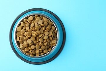 Dry pet food in feeding bowl on light blue background, top view. Space for text
