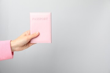 Woman holding passport in bright cover on grey background, closeup. Space for text