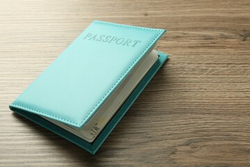 Passport in bright turquoise cover on wooden table, space for text