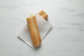Paper bag with fresh baguette on white marble table, top view