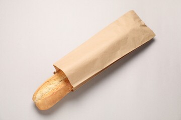 Paper bag with fresh baguette on beige background, top view