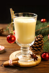 Tasty Christmas cocktail (eggnog) in glass, festive decor and burning candle on wooden table, closeup