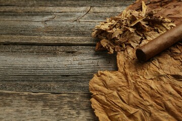 Dried tobacco leaves and cigar on wooden table, closeup. Space for text