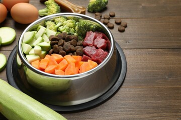 Dry and natural pet food in feeding bowl among products on wooden table, closeup. Space for text
