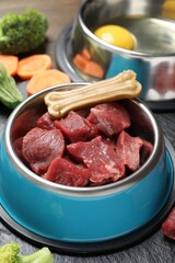 Pet food. Fresh beef in feeding bowl and chew bone on dark textured table, closeup