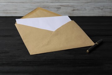 Kraft paper envelope with letter on black wooden table. Mockup for design