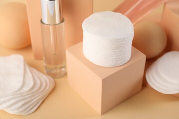 Clean cotton pads and cosmetic products on beige background, closeup
