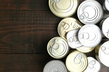 Many closed tin cans on wooden table, flat lay. Space for text