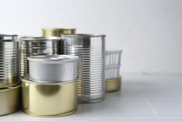 Many closed tin cans on white tiled table, closeup. Space for text