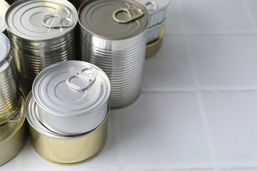 Many closed tin cans on white tiled table, closeup. Space for text