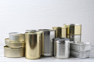 Many closed tin cans on white wooden table, closeup