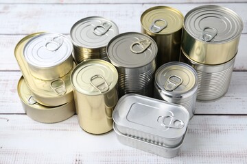 Many closed tin cans on white wooden table, closeup