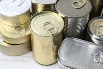 Many closed tin cans on white wooden table, closeup