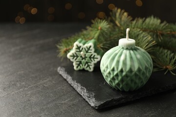 Soy candles in shape of snowflake and Christmas ball among green fir branches on grey table, closeup. Space for text