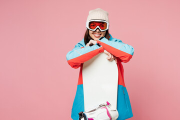 Snowboarder young happy woman wear warm blue padded jacket ski goggles mask spend extreme weekend winter season in mountains hold snowboard look camera isolated on plain pink background Hobby concept