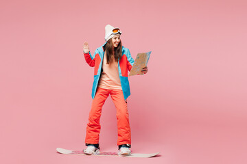 Full body young smiling happy woman she wear warm blue padded jacket ski goggles mask spend weekend winter season in mountains ride snowboard read map isolated on plain pink background. Hobby concept.
