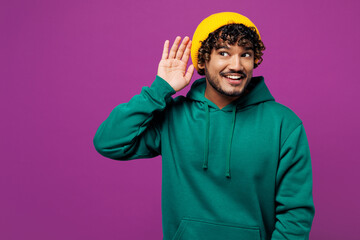 Young curious nosy happy Indian man he wears green hoody yellow hat casual clothes try to hear you...
