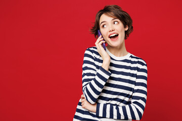 Young happy woman she wear blue striped sweatshirt casual clothes talk speak on mobile cell phone conducting pleasant conversation isolated on plain red background studio portrait. Lifestyle concept.