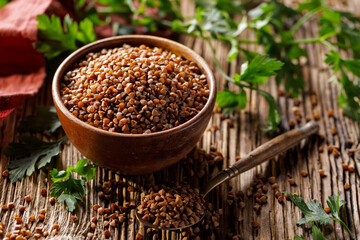 Common roasted brown buckwheat groats in a wooden bowl, close up view