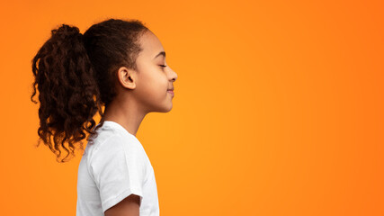 Side view profile portrait of African American girl in white t-shirt posing with closed eyes and curly ponytail hair isolated on yellow studio background wall. Empty free copy space, banner, panorama © Prostock-studio