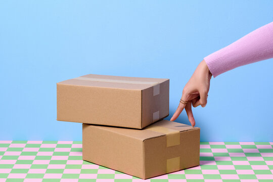 Hand Touching Cardboard Boxes on Colorful Checkered Surface