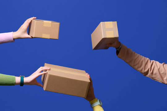 Hands Holding and Exchanging Cardboard Boxes Against Blue Background