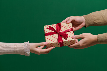 Hands Exchanging Gift Box with Red Ribbon on Green Background