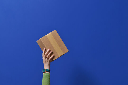 Hand Holding Cardboard Box Against Vibrant Blue Background