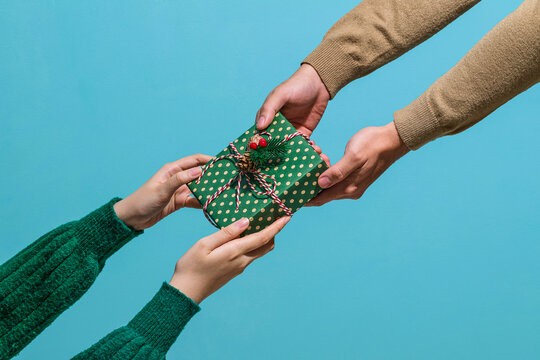 Hands Exchanging a Wrapped Gift Against Blue Background