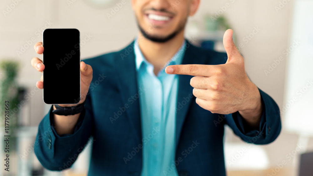 Aufkleber cheerful young arab businessman pointing at smartphone with blank screen at modern office, mockup fo