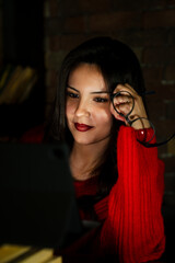 A woman is sitting in a dimly lit room, looking at a computer screen