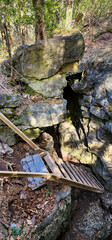 Wooden ladder into a dark rocky crevice with large granite rock, under coniferous trees. 