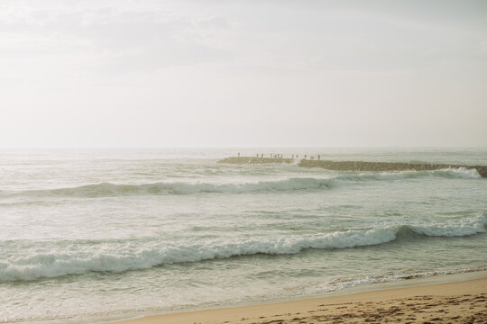 Winter beach with wavy ocean and distant figures on a breakwater