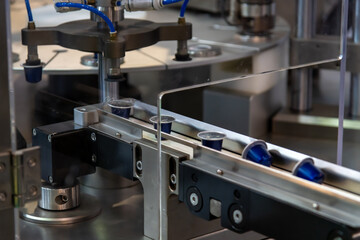 Close-up view of modern coffee pods making machine. Group of blue coffee capsules moves on narrow conveyer belt. Soft focus. Copy space. Coffee manufacturing plant theme.
