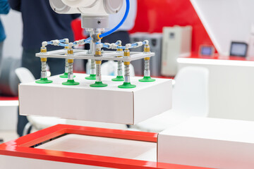 Close-up view of modern white and green vacuum robotic arm manipulator moving white cardboard box...