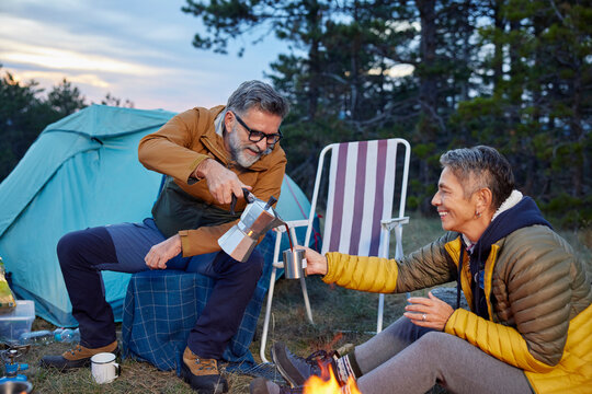 Man serves coffee to a woman in a camp