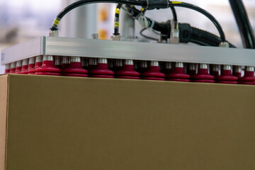 Close-up view of modern grey and red vacuum robotic arm manipulator moving cardboard box in...