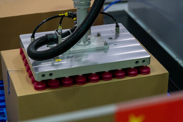 Close-up view of modern grey and red vacuum robotic arm manipulator moving cardboard box in...