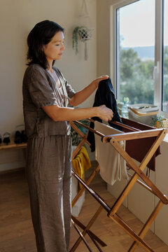 Woman hanging clothes on drying rack at home