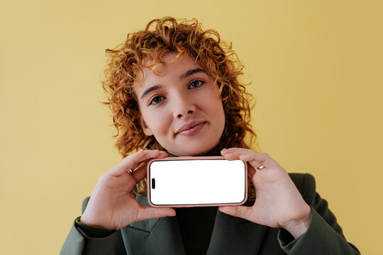 Woman showing smartphone with blank screen on yellow background