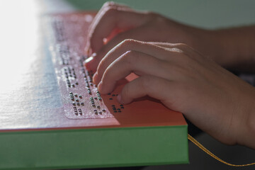 Hands of a little blind child reading the title of a book in Braille