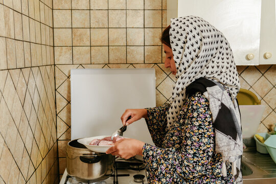 Afghan woman adding lamb cuts into a pressure cooker